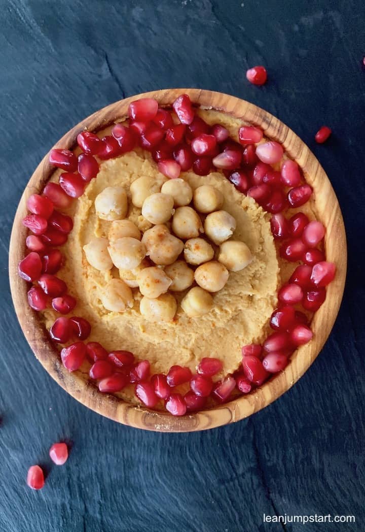 spicy hummus with pomegranates in a wooden bowl