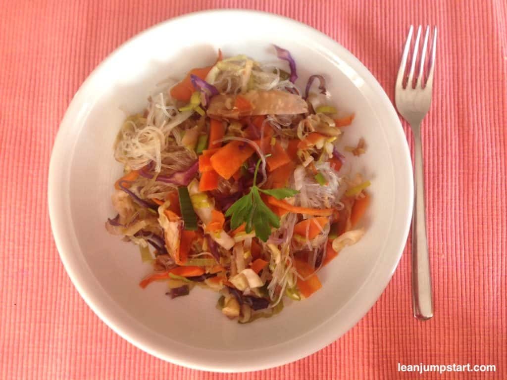 Chinese vegetable stir fry arranged on a white plate with fork on an orange table set.