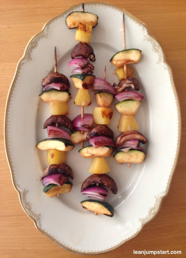 grilled veggie skewers on a white plate with golden border