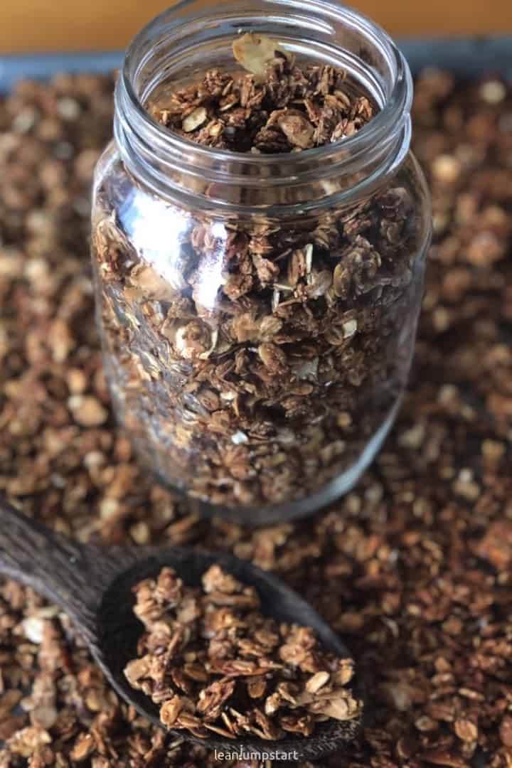 homemade granola in jar with spoon and grains in background