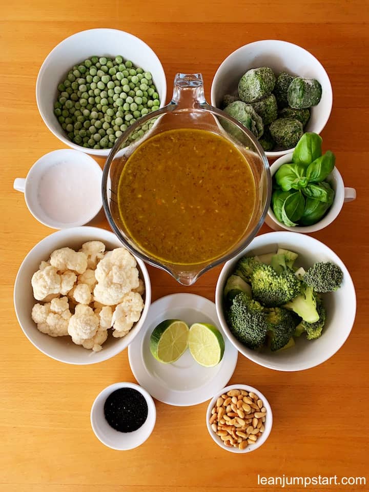 top view of broccoli soup ingredients like broth, frozen spinach, frozen peas, coconut milk, cauliflower, broccoli. basil springs and pine nuts 
