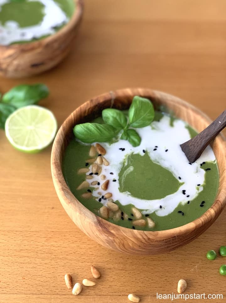 creamy plant-based broccoli soup with spinach and topping in a wooden bowl with a wooden spoon