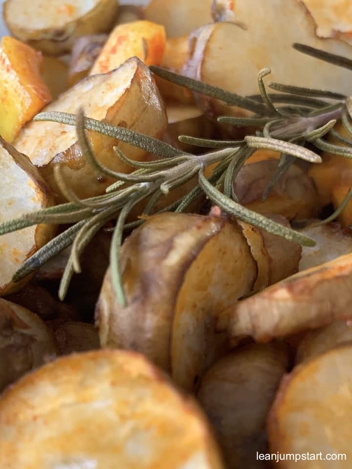 close up of golden brown oven roasted sunchokes with a rosemary stalk on top
