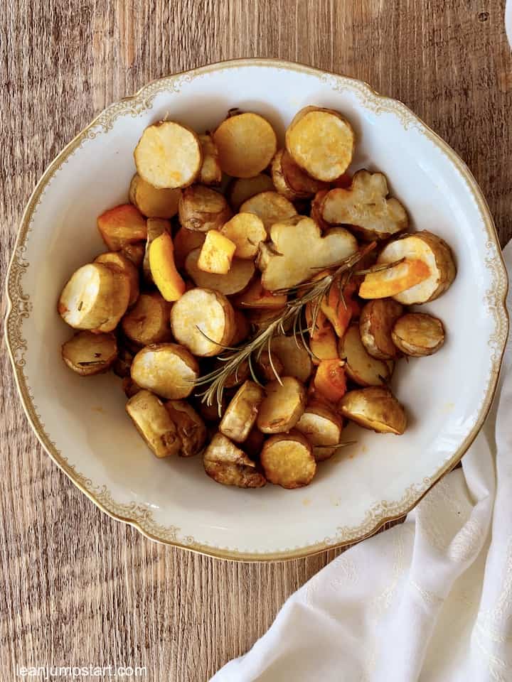 a white plate with golden boarder filled with roasted sunchokes and garnished by a rosemary stalk